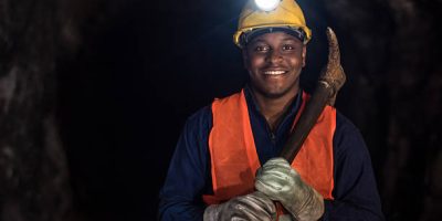 Assistance géologique Happy African American miner working at a mine underground and wearing a helmet with a light