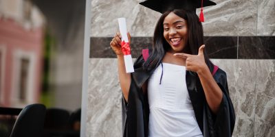 Young female african american student with diploma poses outdoors.
