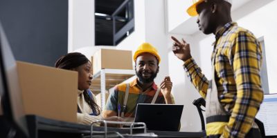 African american logistics managers team dicussing goods distribution at warehouse reception. Post office men and woman workers planning stock supply while chatting at counter desk